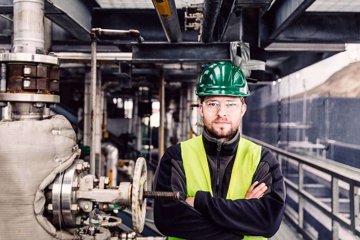 Portrait of manufacturing professional. Manual worker standing with arms crossed by machine. He is in protective wear.